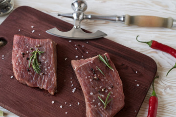 Fresh raw steaks with rosemary and pepper on wooden desk
