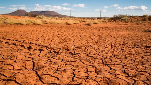 A linear timelapse, pull back dolly shot in a dry semi desert Karoo landscape with dried up abstract, cracked mud with scattered clouds against a blue sky