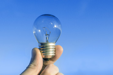 Concept idea of a burning incandescent lamp in a hand against a clear blue sky background from solar energy power