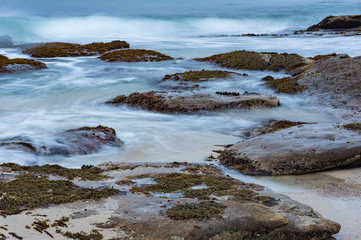 Long exposure shot of waves over rocks and sand