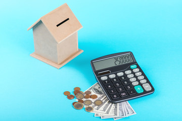 The concept of financial savings to buy a house. Money box, dollars, coins and calculator isolated on blue background.