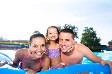 Mother, father and daughter in swimming pool. Sunny summer.