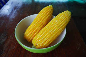Boiled corn cobs in white bowl on wood table.