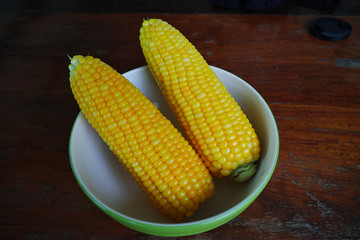 Boiled corn cobs in white bowl on wood table.