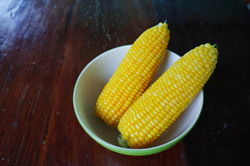 Boiled corn cobs in white bowl on wood table.