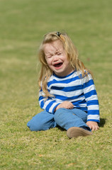 Unhappy cute baby boy sitting on green grass in park