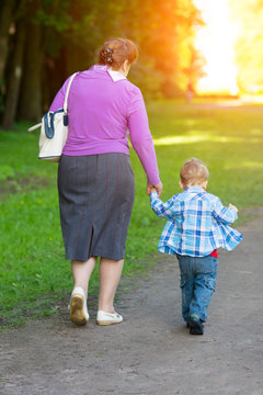 Grandmother walking with her grandson by the hand in the park.