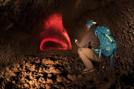 Man exploring an underground lava cave at Etna volcano
