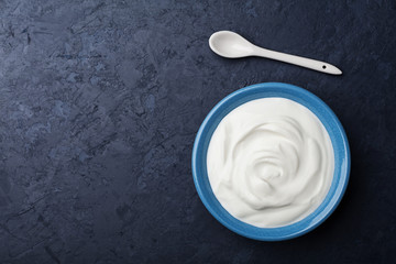 Greek yogurt in blue bowl on black table top view.