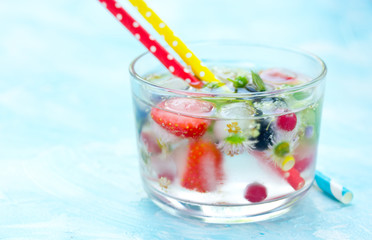 Refreshing water with frozen in ice cubes berries fruits and flowers in glass