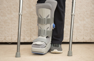 Unrecognisable woman wearing a medical orthopaedic boot with crutches - obrazy, fototapety, plakaty