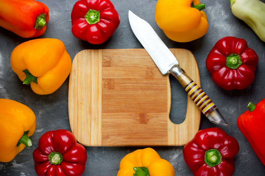 Colorful sweet pepper on table with empty cutting board and knife