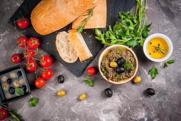 Homemade traditional Italian appetizer tapenade from green and black olives, white ciabatta, fragrant herbs and oil, fresh tomatoes. On a concrete gray table, copy space top view
