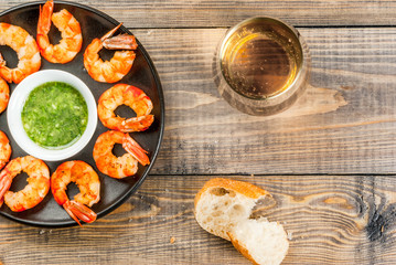 Seafood. Shellfish. Fried grilled shrimp prawns on a plate, with a sauce of olive oil and fresh herbs, with fresh baguette and a glass of wine. Snack, appetizer. On wooden table, top view, copy space