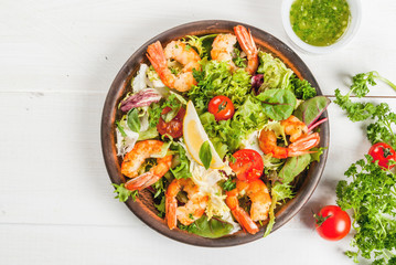 Seafood. Shellfish. Fresh lettuce salad with tomatoes, herbs and grilled fried shrimps prawns, on wooden white table, copy space 