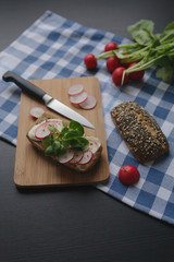 Sandwich with mozarella cheese and slices radish on wooden brown cutting board. Raw vegetables on blue cell lined tablecloth. Food photo.