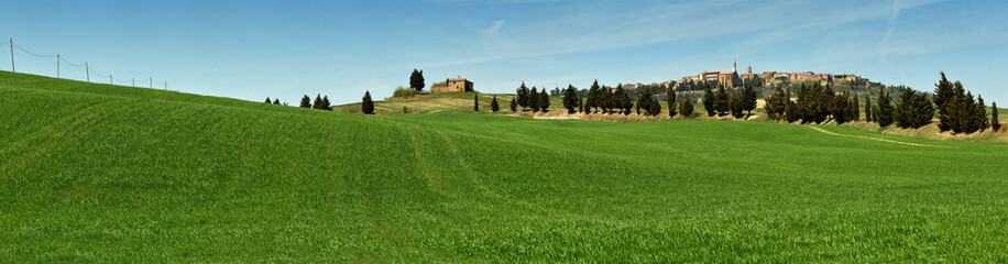 Fototapeta na wymiar PIENZA, TUSCANY / ITALY - MAR 31, 2017: beautiful landscape, with green rolling hills and tuscan cypress trees with Medieval Village of Pienza on background. Located in Siena countryside. Italy.