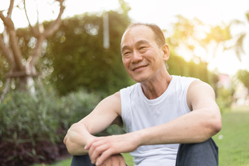 Portrait of Asian senior man relaxing and sitting on grass at the park. Happiness, smiling.