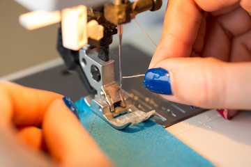needlework and hand quilting in the workshop of a tailor - close-up on tailor fingers with a manicure stick the thread in the needle of the sewing machine. Hobby and sewing concept.