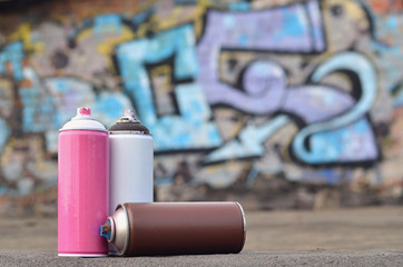 A still-life of several used paint cans of different colors against the graffiti wall