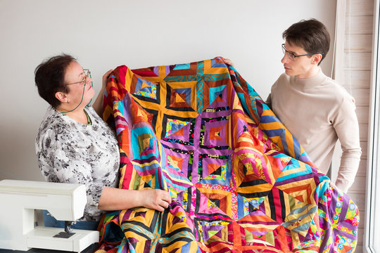 quilting workshop of tailors - male and female tailors together holding in their hands a large weaving product, made from scraps of colored fabric on the sewing machine. Sewing concept. Family hobby.