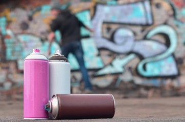 A still-life of several used paint cans of different colors against the graffiti wall