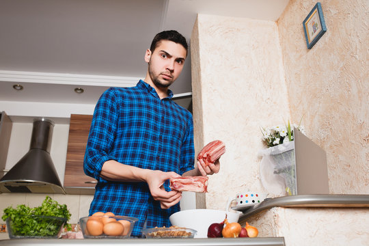 young man preparing meat in her kitchen , looking into the frame