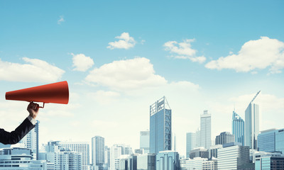 Naklejka premium Hand of businesswoman holding red paper trumpet against cityscape background