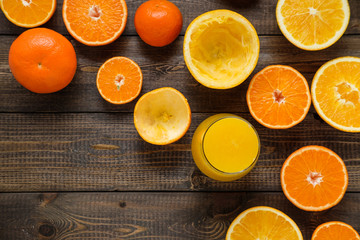 A glass of juice and cut oranges and mandarins on the wooden background