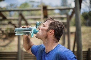 Fototapeta na wymiar Man drinking water from bottle during obstacle course