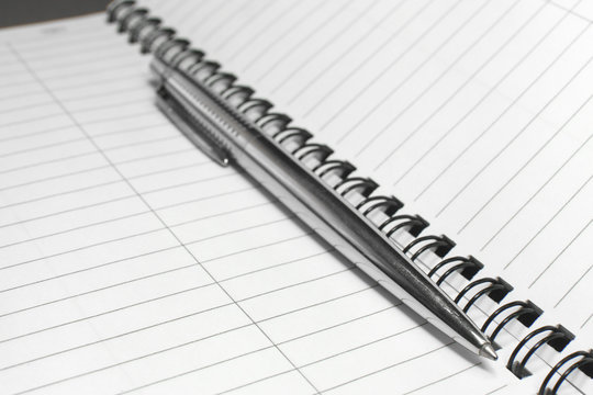 Metallic ball pen on office spiral notebook (manual focus on the pen tip) close up