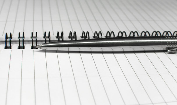 Metallic ball pen on office spiral notebook (manual focus on the pen tip) close up