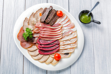 Meat plate with delicious pieces of sliced ham, cherry tomatoes, herbs, meat and sauce. Top view