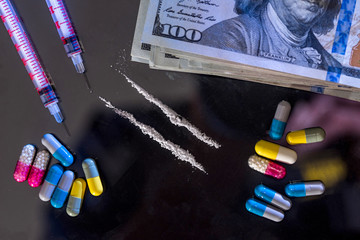 syringe with  heroine, pills, us money isolated on black glass.