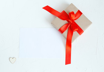 Holiday Post card with heart and copy space Beige gift box with red ribbon. White stone background 