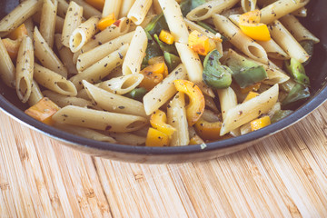 Mediterrane Nudelpfanne mit Penne und bunten Paprika, auf Bambusholz