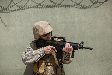 Fototapeta premium Military soldier aiming with a rifle against concrete wall