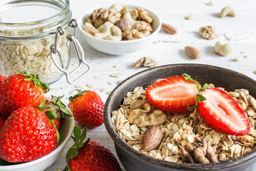 bowl of oat muesli with strawberry, granola and nuts on rustic wooden table