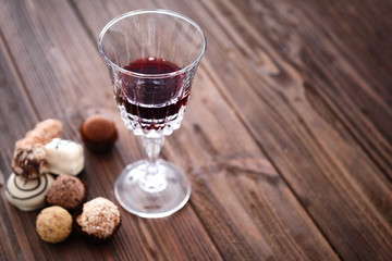 Glass of red wine and chocolates on wooden background