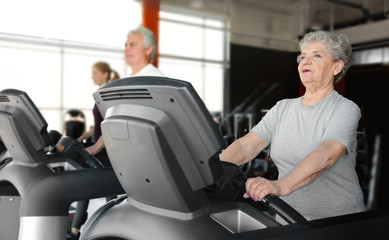 Fototapeta na wymiar Senior woman running on treadmill in gym