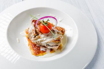 Fototapeta na wymiar Tasty roasted pork pieces with cheese sauce, tomato and onion on white plate close up. Selective focus image
