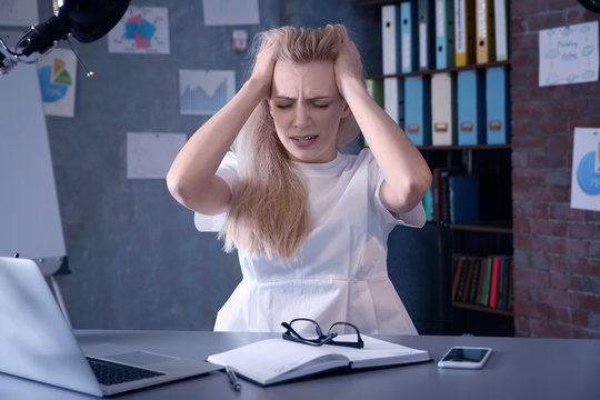 Beautiful young woman suffering from headache while working in office