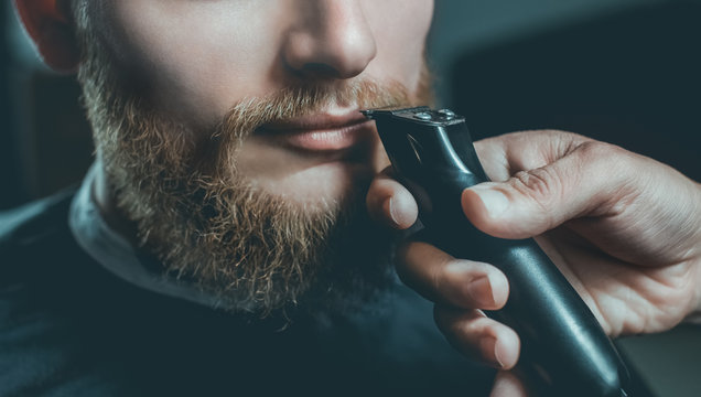 A male hairdresser does a haircut of a beard and a mustache in a barbershop.