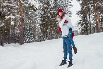 Fototapeta na wymiar Love - Happy couple having fun smiling happy laughing together on romantic holidays. Young man giving piggyback ride to his girlfriend outdoor in winter park.
