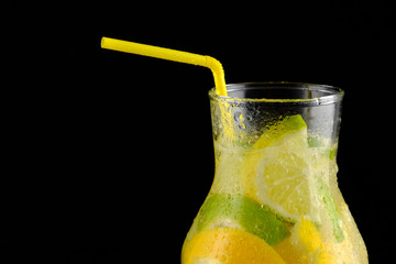 Decanter with soda water, lemons and a straw on a black background.