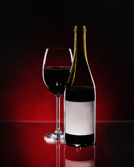 Red vine on glass and bottle on gradient mirror table or background.