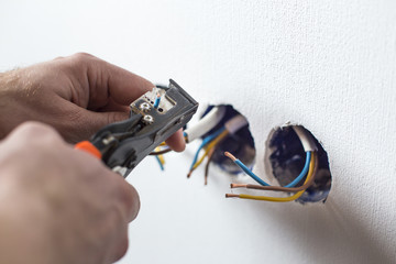 Pliers peeling copper wires. Сloseup on electrician hands, wall sockets in the background