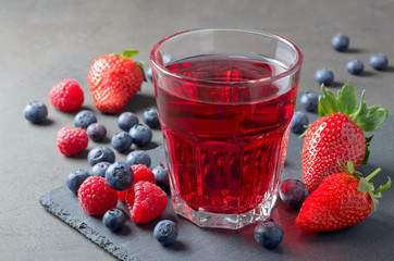 Glass of juice made of raspberries, strawberries and blueberries on a slate plate