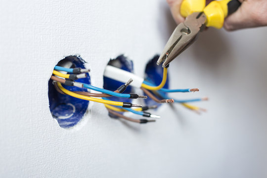 Electrician mounting the wires into electrical wall fixture or socket, closeup on hands and pliers