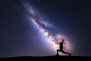 Foto op Plexiglas Milky Way with silhouette of a standing woman practicing yoga on the mountain. Beautiful landscape with meditating girl against night starry sky with milky way. Amazing galaxy. Universe. Fitness © den-belitsky